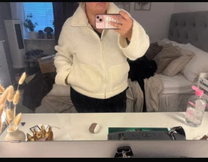 Vit teddyjacka från 157 - Mysig vit teddyjacka från 157 med dragkedja framtill och två stora fickor. Jackan har hög krage och är tillverkad i fluffigt teddy-material som håller dig varm. Perfekt för kyliga dagar och har en avslappnad passform med långa ärmar.