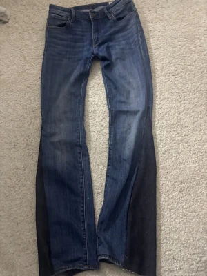 Bootcut jeans - Säljer ett par snygga blå Levi's jeans med bootcut passform. Jeansen har klassisk femficksdesign, mörkare paneler längs utsidan av benen och en läderpatch med Levi's-logga bak. Tillverkade i slitstarkt denimtyg med lätt tvättad look. strl 28/32 den har hål vid knäna 