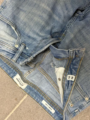 Jack & Jones ljusblåa jeans  - Säljer ett par ljusblå jeans från Jack & Jones med klassisk femficksdesign och snygga slitningar. Jeansen har gul kontrastsöm och är tillverkade i mjukt denimtyg som sitter bra längs benen. 