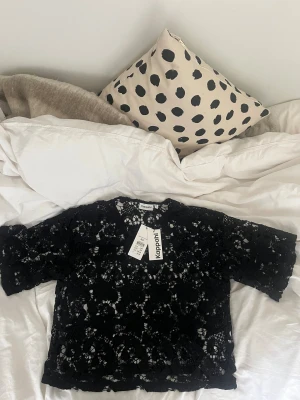 Svart spetsblus från Kappahl XS - Säljer en svart blus från Kappahl i storlek XS. Blusen har ett detaljerat blommigt spetsmönster och är kortärmad med rund hals. Perfekt för dig som gillar statement-plagg med coola detaljer och snygg struktur.