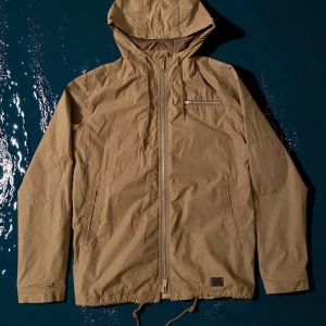 Beige vindjacka från Brixtol - Skitsnygg beige vindjacka från Brixtol med huva och snörning i nederkant stl S. Jackan har dragkedja framtill, en bröstficka med zip och två sidofickor. Varsamt använd och är i väldigt bra skick.