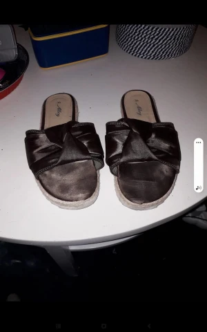 Bruna satinsandaler från Alley, strl 36 - Snygga bruna sandaler från Alley i satin med bred knutdetalj över foten. Platt sula med repdetalj runt kanten ger en chill vibe. Perfekta för sommardagar när du vill vara både bekväm och trendig.