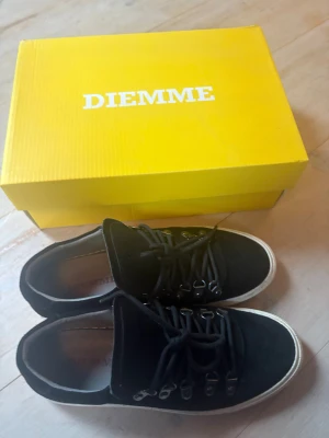 Svarta mockasneakers från Diemme - Svarta sneakers från Diemme med ovandel i mocka och robust snörning med metallöglor. Skorna har vit platt sula och rund tå, vilket ger en clean och stilren vibe. Perfekt för dig som gillar italiensk design och vill ha något som sticker ut. Lite smutsig sula men inga andra tecken på användning.