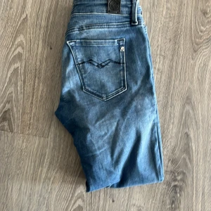 Replay Anbass skinny jeans blå - Säljer ett par Replay Anbass jeans i klassisk blå tvätt med snygga slitningar. Jeansen har skinny fit, fem fickor och detaljerad bakficka med broderad våg. Metallknapp och dragkedja framtill. Perfekta för dig som gillar en tajt passform och stilren look. Kan gå ner i pris 