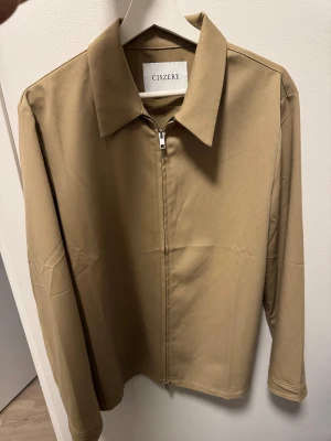 Beige overshirt från Ciszere - Stilren beige overshirt från Ciszere med klassisk krage och dragkedja framtill. 