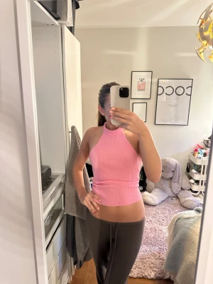 Rosa ribbad halterneck topp - Säljer en rosa ribbad halterneck topp med knyt i nacken och öppen rygg. Toppen är croppad och ärmlös. Materialet är mjukt och stretchigt, vilket gör den skön att bära.