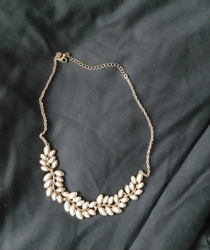Guldigt halsband med pärldetaljer - Snyggt halsband i guldton med dekorativa pärlor formade som blad. Kedjan är tunn och har ett justerbart lås. Perfekt för dig som gillar unika smycken med naturinspirerad design. Bladformen ger en cool och elegant vibe.