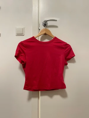 Röd croppad topp med kort ärm - Säljer en enkel och snygg röd croppad topp med rund hals och korta ärmar. Toppen är slät utan mönster och har en klassisk passform som sitter lite tight. Perfekt att matcha med jeans eller kjol för en cool look.