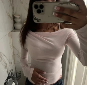 Ljusrosa offshoulder topp - Säljer en ljusrosa långärmad topp med offshoulder-design. Toppen är tight och har en snygg omlottkänsla över bysten. Tillverkad i ett tunt och stretchigt material som sitter skönt mot kroppen. Perfekt att styla med jeans eller kjol.