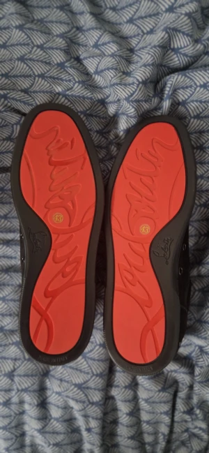 Svarta sneakers från Christian Louboutin - (Dem är helt nya och oanvända)Säljer ett par svarta sneakers från Christian Louboutin med ikoniska röda sulor och signaturdetaljer på sidan. Skorna har snörning, rund tå och är tillverkade i mocka med inslag av skinn. Snygg och stilren design som sticker ut med den röda undersidan.