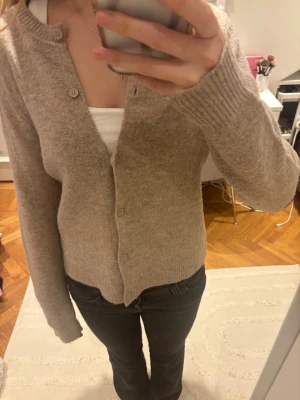 Beige kofta - Mysig beige kofta med rund hals och knäppning framtill. Tröjan har långa ärmar och ribbade muddar vid ärmslut och nederkant. Perfekt att slänga på sig när det är lite kyligt ute. Enkel och stilren design som funkar till många olika outfits.