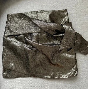 Metallic kortkjol från Mango, strl M - Metallic kortkjol från Mango i storlek M. Kjolen har en glittrig, guld-brun yta med struktur och bred linning. Materialet är syntet och kjolen har en omlottliknande detalj framtill. 