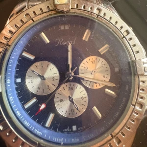 Regal herrklocka med blå urtavla - Snygg klocka från Regal med blå urtavla och tre silvriga subdials. Boetten och länken är i silverfärgat metall och har en sportig design med markerade siffror på ringen. Perfekt för dig som gillar klassisk stil med lite edge.