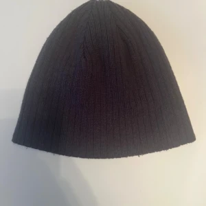 Mörkgrå ribbad mössa från Trend Eagle för ungdomar - En mörkgrå, ribbstickad mössa från Trend Eagle. Klassisk och enkel design i one size som passar ungdomar. Tillverkad i 100% akryl.