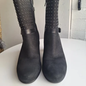 Svarta boots med nitar från Ecco - Snygga svarta boots från Ecco i skinn med dekorativa nitar framtill och två spännen på sidan. Skorna har en stadig klack, rund tå och dragkedja på insidan för enkel påtagning. Perfekta för dig som vill ha en edgy men stilren look.