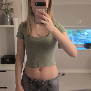 Grön magtröja med urringning - Snygg ljusgrön croppad topp med rundad halsringning och korta ärmar.  Enkel och stilren design som är lätt att matcha med jeans eller kjol. Mjuk och skön bomullskvalitet som passar perfekt för varmare dagar. Perfekt för dig som gillar en chill och trendig look. Det är några små fläckar nere på tröjan men som säkert går bort i tvätten.