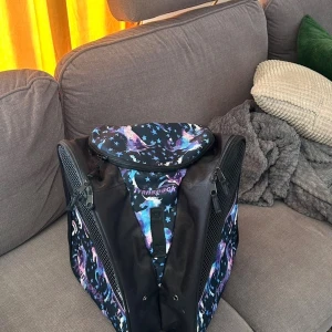 Skridskoväska från Transpack ryggsäck med enhörningar - Cool ryggsäck från Transpack med svart bas och färgglatt enhörningsmönster i blått, lila och rosa. Väskan har flera fack, meshpaneler på sidorna och dragkedjor. Perfekt för dig som vill sticka ut med en unik och praktisk väska. Passar perfekt till skidskor. 