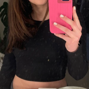 Svart croppad långärmad topp - Säljer en svart, croppad långärmad topp med rund halsringning. Toppen är ribbad och har en tight passform som framhäver figuren. Perfekt att styla med höga jeans eller kjol för en trendig look.