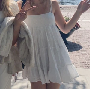 Zara klänning - Säljer en söt vit kort klänning med tunna axelband och volanger. Klänningen har en smockad överdel och ett luftigt, flowy tyg som ger en chill vibe. Perfekt för varma dagar och häng vid vattnet. Fråga gärna om fler bilder eller mått!