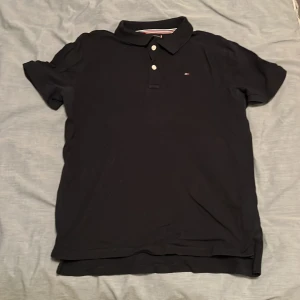 Blå pikétröja Tommy Hilfiger - Blå pikétröja från Tommy Hilfiger med klassisk krage och tre vita knappar framtill.