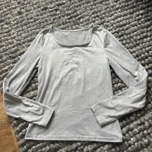 Ljusgrå långärmad topp - En stilren ljusgrå långärmad topp med rundad fyrkantig urringning. Tunn och mjuk i materialet, perfekt att styla med jeans eller kjol. Enkel design som funkar till många looks.