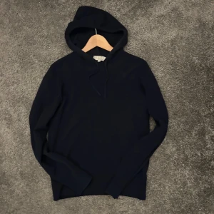 Kashmir hoodie  - Mysig mörkblå hoodie från Carmes i lyxig kashmir. Tröjan har huva med snörning och långa ärmar, perfekt för dig som gillar en stilren och enkel look. Passar dig som vill ha något både bekvämt och snyggt till vardags.