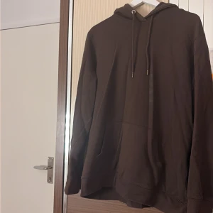 Brun hoodie från 157 i storlek L - Brun hoodie från 157 med klassisk huva och snörning. Tröjan har en stor magficka och ribbade muddar vid ärmslut och nederkant. Perfekt för chill dagar och enkel att matcha med jeans eller mjukisbyxor.