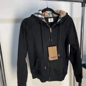 Svart Burberry hoodie - Svart hoodie från Burberry i väldigt bra skick (nyskick). Den är väldigt stilig och är perfekt för dig som gillar unika plagg😎. 