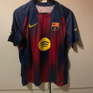 FC Barcelona Rashford 14 Nike tröja - Snygg FC Barcelona matchtröja med Rashford och nummer 14 på ryggen. Tröjan är randig i mörkblått och rött med gula detaljer, klubbmärke och sponsorloggor. Tillverkad i lätt och ventilerande material, perfekt för fotboll eller att bära till vardags.