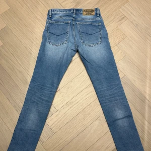 Blå skinny jeans från Crocker - Säljer ett par blå jeans från Crocker med slitna detaljer framtill och klassisk femficksdesign. Jeansen har skinny passform och är tillverkade i mjukt denimtyg med snygga tvättade partier. Perfekt för dig som gillar en modern och avslappnad stil.