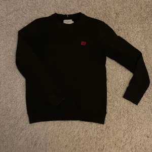 Svart sweatshirt från Les Deux - Svart sweatshirt från Les Deux med rund hals och lång ärm. Tröjan har en liten röd patch med logga på bröstet. Perfekt för dig som gillar stilren och enkel design. 