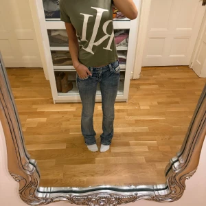 Olivgrön t-shirt från Ralph Lauren - Snygg olivgrön t-shirt från Ralph Lauren med stor vit RL-logga framtill. Klassisk rund halsringning och korta ärmar. Skön passform i mjuk bomull, perfekt till jeans eller shorts för en avslappnad look.