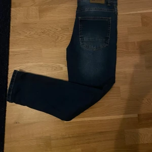 Blå relaxed jeans från Tumble 'N Dry - Snygga blå jeans från Tumble 'N Dry med relaxed passform. Klassisk femficksmodell med tydliga kontrastsömmar och knappstängning framtill. Jeansen har en mörk tvätt och är tillverkade i slitstarkt denim-material. Aldrig andvända