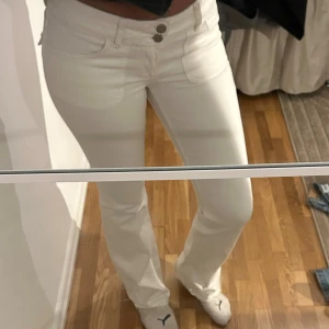 Vita bootcut jeans med fickdetaljer - Snygga vita jeans med bootcut passform och hög midja. Framtill finns dubbla knappar och klassiska fickor, baktill två fickor med lock och silverknappar. Jeansen har en stilren look och är gjorda i stretchig bomull för skön passform.