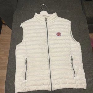 Vit dunväst från Colmar - Snygg vit dunväst från Colmar med quiltad design och hög krage. Västen har två fickor med dragkedja och en tydlig Colmar-logga på bröstet. Perfekt för lager-på-lager och enkel att matcha med olika outfits. Priset kan alltid diskuteras via snabba affärer 