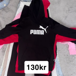Svart hoodie från Puma med logga - Svart hoodie från Puma med stor vit logga på bröstet. Tröjan har huva med snörning och en klassisk magficka framtill. Perfekt för dig som gillar sportig och avslappnad stil.