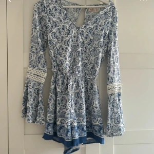 Blåvit kortklänning (shorts nertill) från Hollister XS - Supersöt blåvit kortklänning/jumpauit från Hollister med långärmade trumpetärmar och v-ringning. Klänningen har ett vackert blommigt mönster, markerad midja och spetsdetaljer på ärmarna. Perfekt för sommarens alla tillfällen!