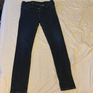 Mörkblå skinny jeans  - Snygga mörkblå jeans med klassisk femficksdesign och smal passform. Jeansen har knappgylf och är tillverkade i stretchigt denim som sitter tajt längs benen. Perfekta för dig som gillar en stilren och modern look. W33 L32