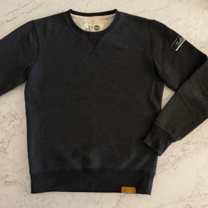 Mörkgrå sweatshirt från Solid, S - Mysig mörkgrå sweatshirt från Solid med mjukt fleecefoder på insidan. Tröjan har rund hals, ribbade muddar och en snygg patch med logga på ärmen. Perfekt för dig som gillar enkel och stilren design med lite streetkänsla. Perfekt skick. 