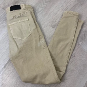 Beige skinny jeans från FitJeans - Snygga beige jeans från FitJeans med smal passform och klassisk femficksdesign. Byxorna har dragkedja och knapp framtill, samt ett svart lädermärke med logga bak i midjan. Perfekt för dig som gillar stilrena och tajta jeans.