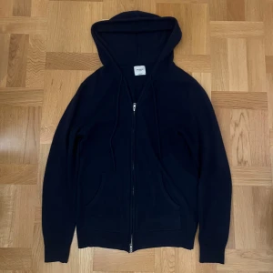 Mörkblå hoodie i kashmir från John Henric - Svart hoodie från John Henric i mjuk kashmir. Tröjan har huva med snörning, dragkedja framtill och två fickor. Långärmad och med en clean, klassisk look som funkar till chill och streetwear. Perfekt för dig som gillar stil och komfort. Kom med frågor om pris eller hoodien i sig👍