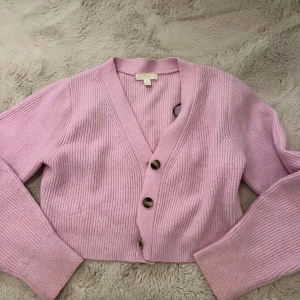 Ljusrosa ribbad kofta från H&M - Superfin ljusrosa kofta från H&M i ribbstickad kvalitet. Croppad modell med v-ringning och tre stora knappar framtill.