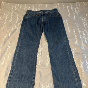 Levi's 501 blå jeans W34 L32 - Klassiska Levi's 501 jeans i blå denim med raka ben och normal passform. Snygga kontrastsömmar, fem fickor och ikonisk läderpatch bak. Perfekta för dig som gillar tidlös stil och vill ha ett par jeans som alltid funkar.