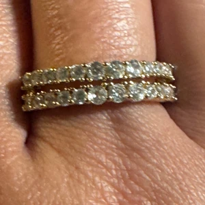 Dubbelradig i 18k guldpläterad med stenar - Snygg dubbelradig ring i 18k guldpläterad med två rader glittrande, runda vita stenar som ger en lyxig och modern känsla. Ringen har en klassisk form och passar perfekt för dig som gillar att sticka ut med bling. Perfekt som statement piece eller att kombinera med andra smycken.