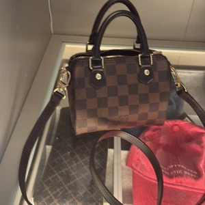  rutig handväska brun💘 - Snygg handväska i klassiskt rutigt mönster, bruna och mörkbruna toner. Väskan har guldfärgade detaljer, dragkedja och avtagbar axelrem. Insidan är röd och materialet är kanvas. Perfekt storlek för det viktigaste och en ikonisk look. Dustbag och original förpackning ingår!🌟tveka inte att höra av er vid minsta fråga!💓