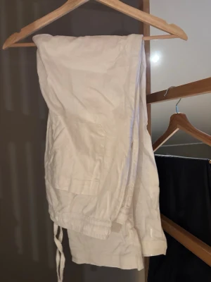 Vita linnebyxor med snörning - Säljer ett par vita linnebyxor med avslappnad passform och snörning i midjan. Byxorna har raka ben och praktiska fickor på sidorna. Perfekta för varma dagar och chill vibes.