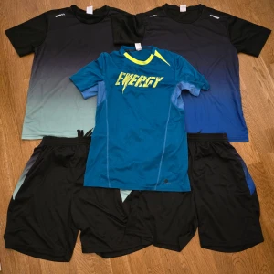 Träningskläder Herr M Svart och Blå/Grön *nyskick* - Hej! Säljer två kompletta träningsset från BURUITE – t-shirt och shorts i lätt, snabbtorkande polyester. Perfekt för gym, löpning eller vardagsaktivitet.  Dessutom ingår en extra t-shirt från Decathlon i polyester med snygg design och bekväm passform.  Färger: Svart, blå, grön. Storlek: M. Allt säljs i paket och är i fint skick – redo att användas direkt.  Mvh, Lucas