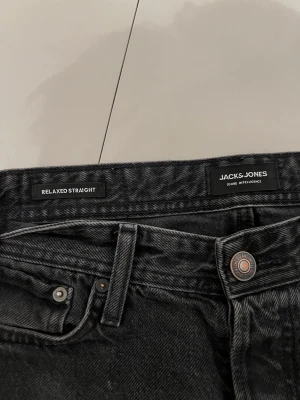 Svarta relaxed straight jeans Jack & Jones - Säljer ett par svarta relaxed straight jeans från Jack & Jones i storlek 29/30. Klassisk femficksmodell med raka ben och normal passform. Jeansen är tillverkade i ett mjukt denimtyg och har metallknapp och nitar. Perfekta för en chill och enkel stil.