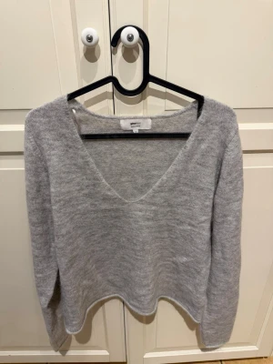 Grå stickad tröja från Gina Tricot - Mysig grå stickad tröja från Gina Tricot med djup v-ringning och långärmad design. 