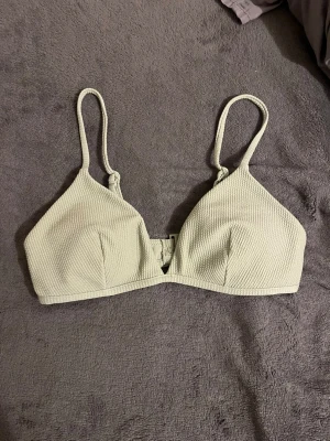 Ljusgrön bikiniöverdel från H&M - Säljer en ljusgrön bikiniöverdel från H&M med smala axelband och strukturmönstrad yta. Modellen har triangelformade kupor och knäpps med spänne i ryggen. Perfekt för strandhäng eller poolen! Storlek 40, men passar även 38or! 